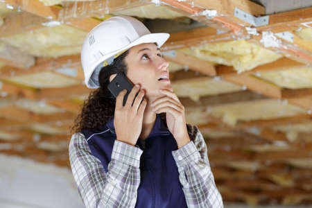 female builder using smartphone to communicate problem with ceilingの写真素材