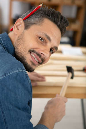 handyman hammering wood with a opencil behind his earの写真素材