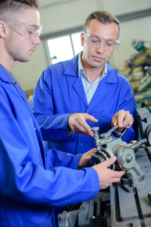 Engineer and apprentice holding mechanical part