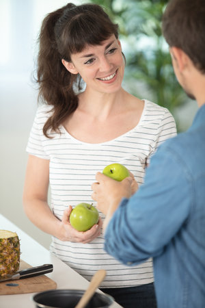young couple together in kitchen holding applesの写真素材