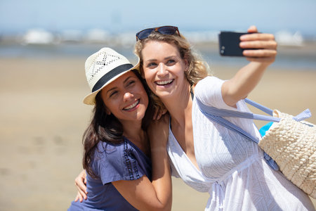 funny female friends on vacation taking selfies on the beach