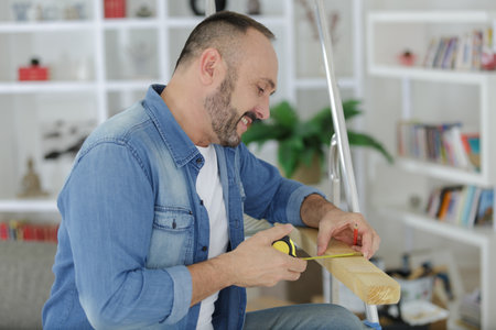 man measures wooden board in his workshopの写真素材