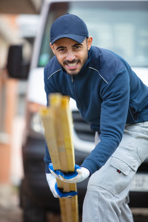 smiling carpenter holding wood planks in a construction site