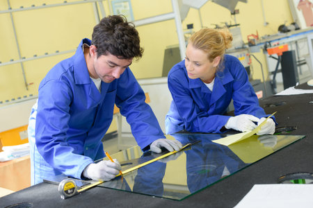 Young workers measuring pane of glass