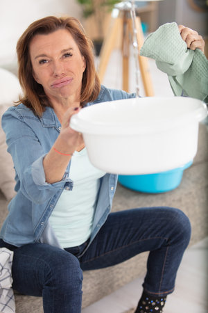 worried mature woman collecting water leakage from ceilingの写真素材