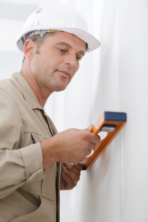 professional worker in helmet is measuring wall with level