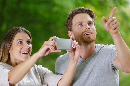 happy young couple looking up in amazement and taking photograph