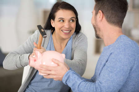young couple breaking piggy bank with hammer at homeの写真素材