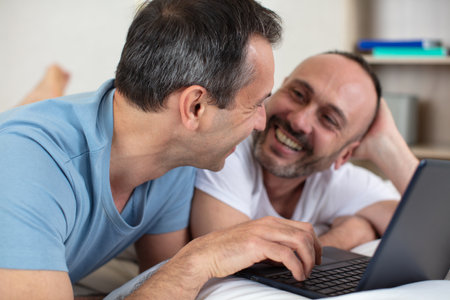 attractive couple lying on bed and using laptop at homeの写真素材