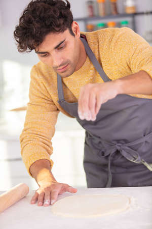 male baker sprinkling flour on pastryの写真素材