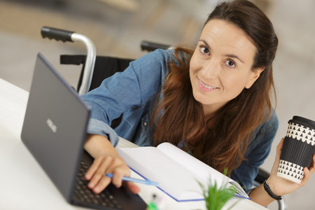 cheerful disabled woman using her laptop while drinking coffee