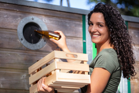 woman putting glass bottle in a green glass recycling container