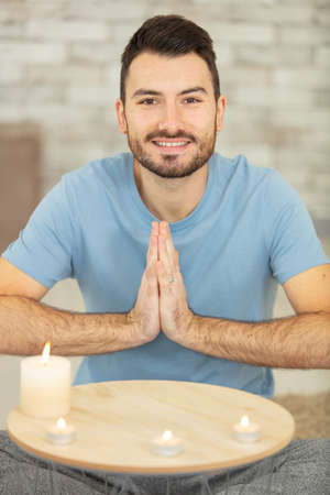 smiling man with hands in prayer position by lit candlesの写真素材
