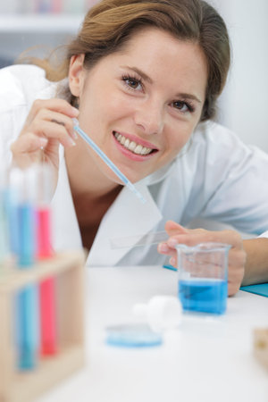 happy woman in lab coat inspecting liquid