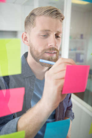 man writing at sticky notes on windowの写真素材
