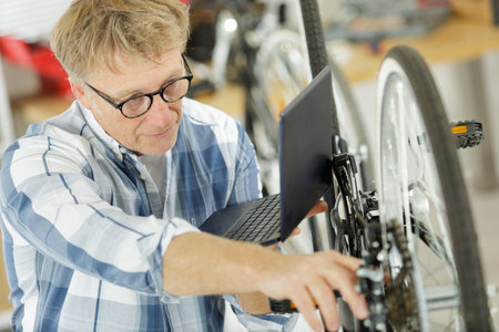 mature man using a laptop for repairing bicycle at homeの写真素材