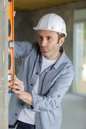 professional worker in helmet is measuring wall with level