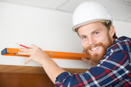 young man using spirit level on white wall