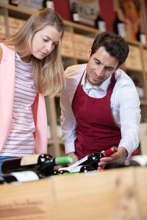 sommelier in wine store giving woman recommendationの写真素材