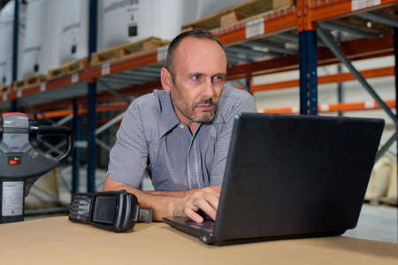 focused warehouse manager working on laptopの写真素材