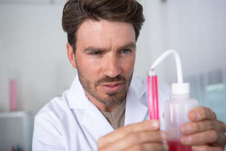 male scientist pouring red liquid from beaker into test tubeの写真素材
