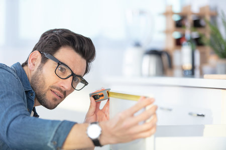 professional young handyman measuring kitchen furniture