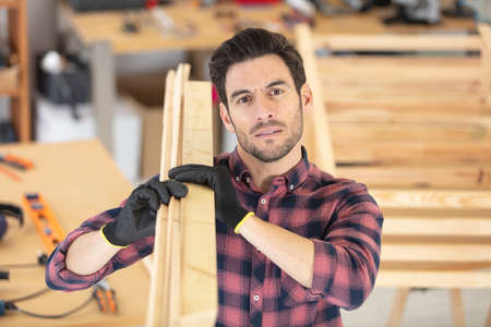 smiling mature carpenter carrying a wooden planks on his shoulderの写真素材