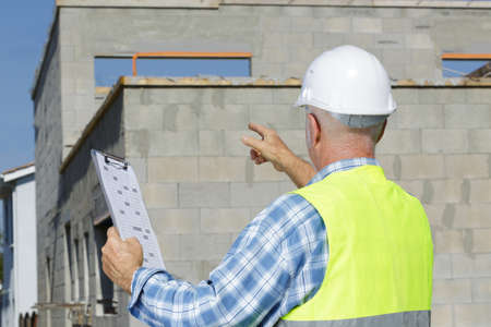 rear view of senior builder on development site holding clipboardの写真素材