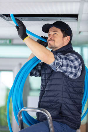 plumber holding a blue pipe above a ceilingの写真素材