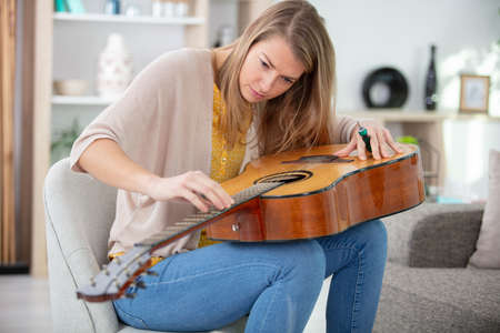young woman tuning guitar at homeの写真素材