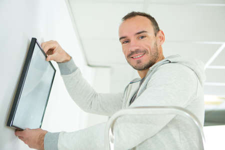 man positioning picture frame on wallの写真素材