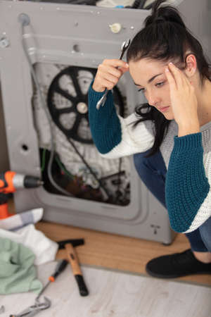 depressed woman with spanner next to broken washing machineの写真素材