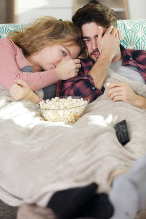 scared couple eating popcorn while watching a horror movieの写真素材