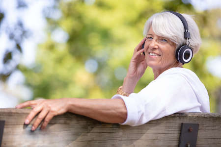smiling elder lady sitting on a bench in the parkの写真素材
