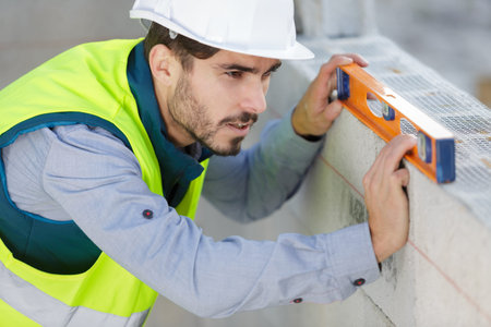 young male builder using a level outdoors