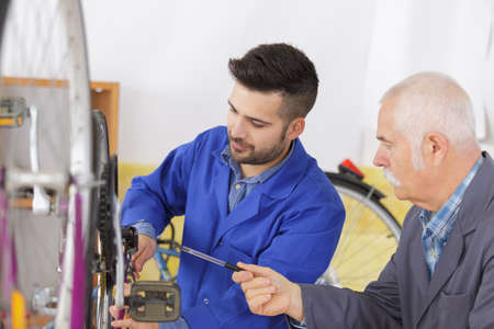bicycle mechanic and apprentice repairing a bike in workshopの写真素材
