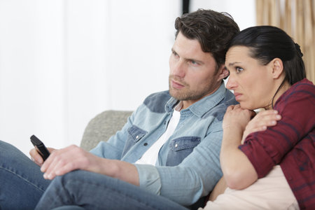 sad couple at home sitting on sofa watching tv