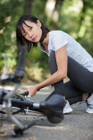 a woman is fixing a bike outdoorsの写真素材