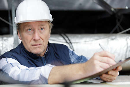 man electrician wiring inside ceiling taking notesの写真素材