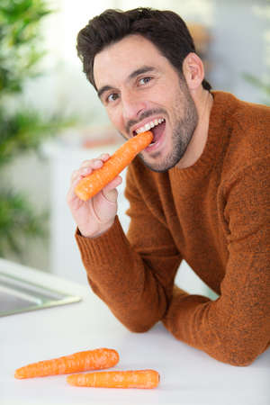 young man is eating a carrot at homeの写真素材