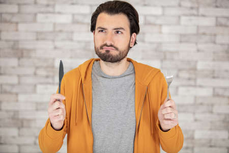 confused man holding a knife and forkの写真素材