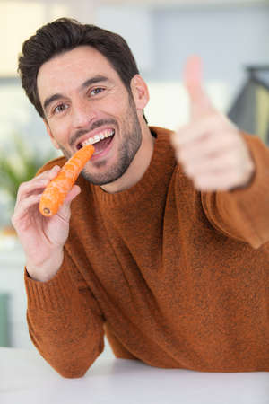 handsome man eating carrot at homeの写真素材