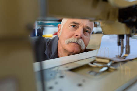 senior mechanic repairing industrial sewing machine in factoryの写真素材