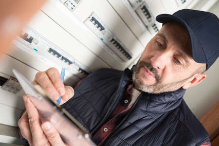 male electrician with clipboard near fuse board indoorsの写真素材