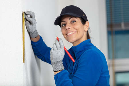 woman builder in uniform measuring wallの写真素材