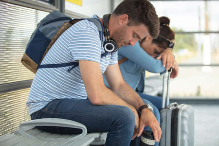 tired couple sitting on bench at the train stationの写真素材