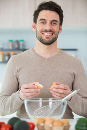 man whisking eggs in bowl for cooking omelet with vegetablesの写真素材