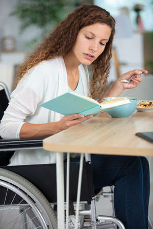 woman in wheelchair at home reading at the tableの写真素材