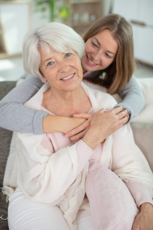 happy young adult hugging her grandmother on the sofa