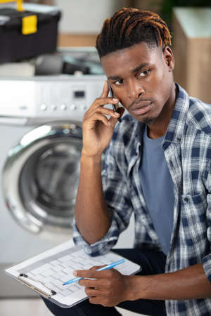 washing machine repairman holding clipboard and talking on smartphoneの写真素材